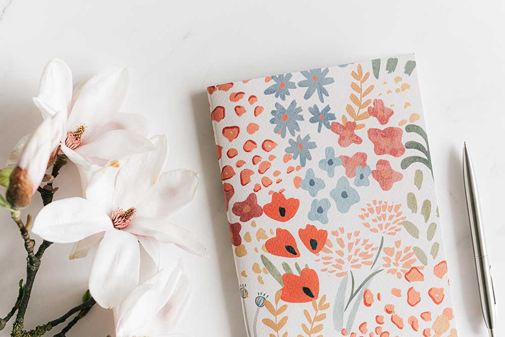 A notebook with floral print laying next to white flowers