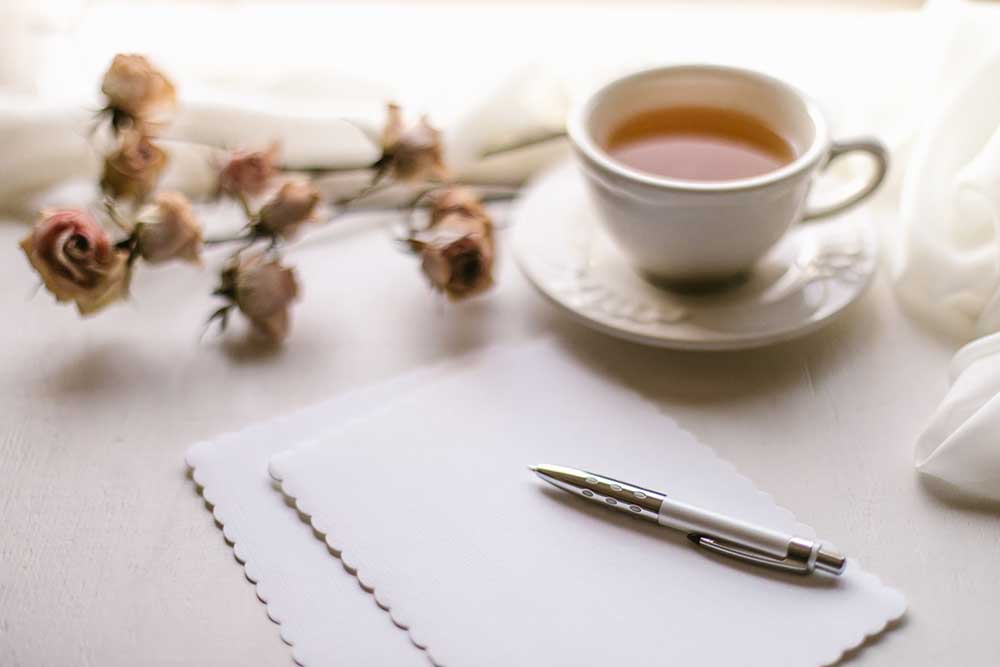 cup of tea next to white blank paper and a pen
