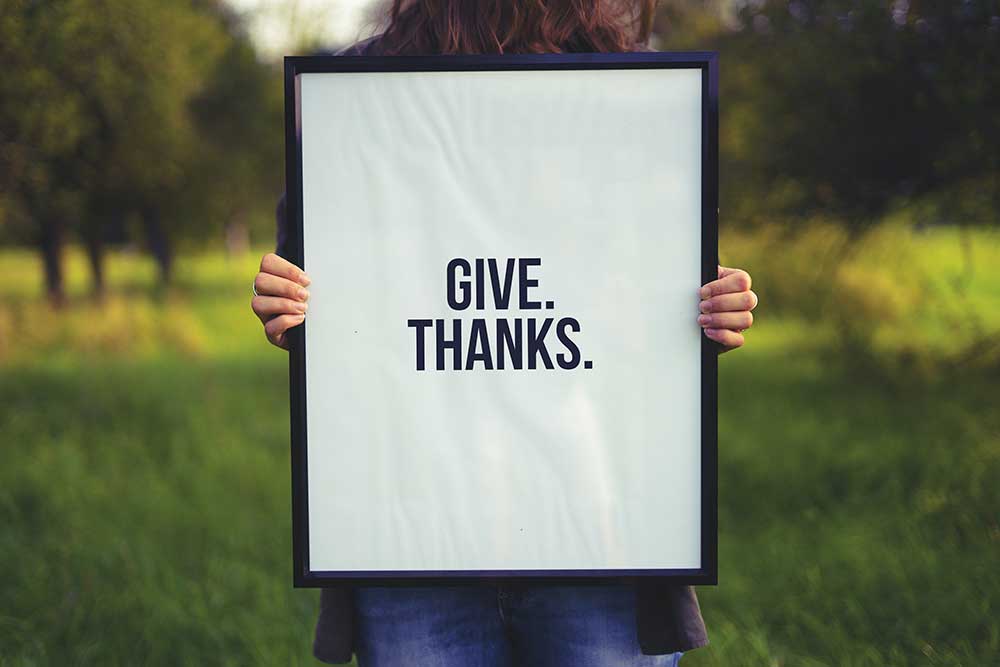Woman holding a sign that says Give Thanks