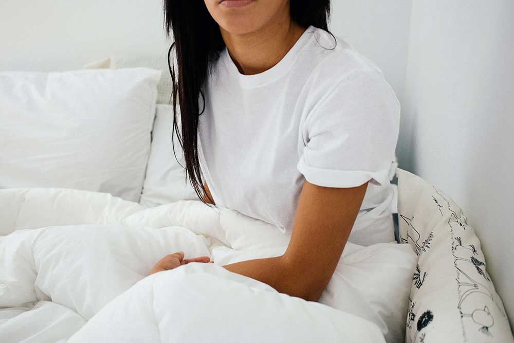 woman sitting up in her bed with white sheets