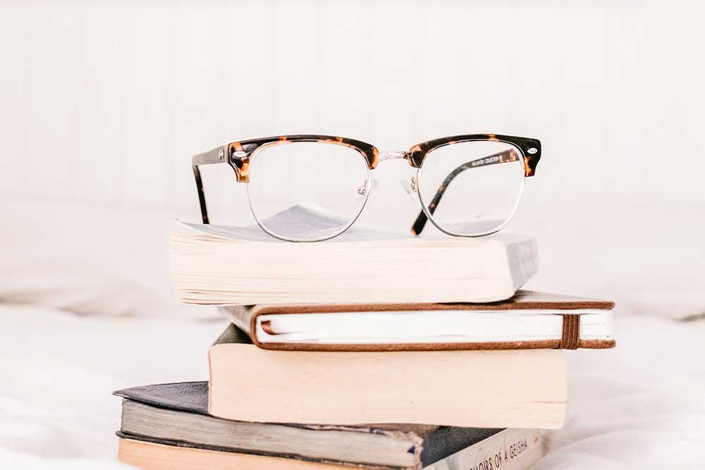 Stack of books on a table with a pair of reading glasses on top