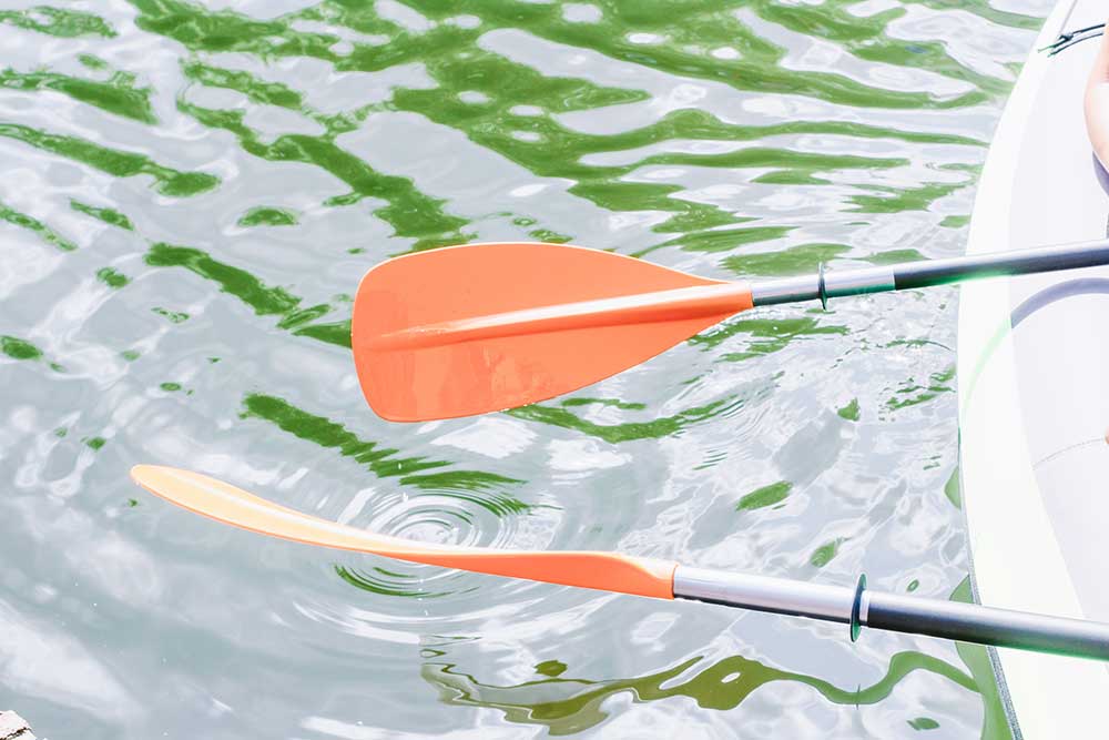 two orange paddles above the water with a kayak