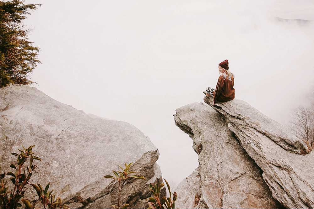 Collide blog girl sitting on the edge of a solid rock cliff with nothing but fog below her
