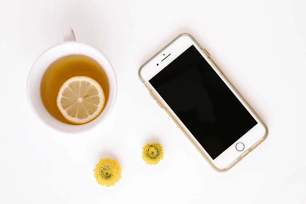 Collide Blog Cup of tea with lemon and phone on table with yellow flower