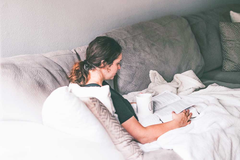 Young Woman Sitting on Couch studying and drinking coffee