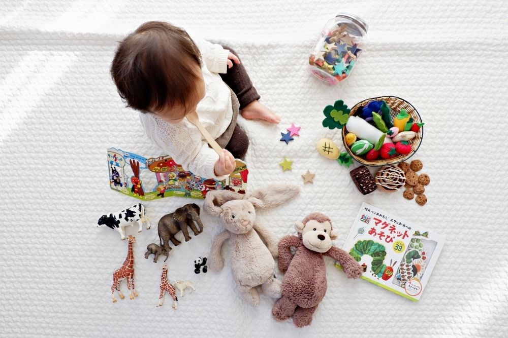 baby sitting on white blanket playing with collection of toys