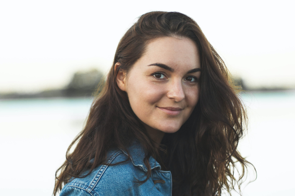 dark haired woman in jean jacket smiling on a beach