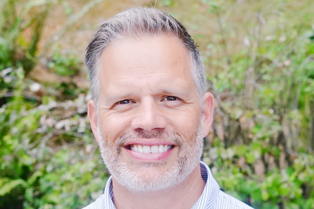 Headshot of pastor Christian Lindbeck smiling with greenery behind him