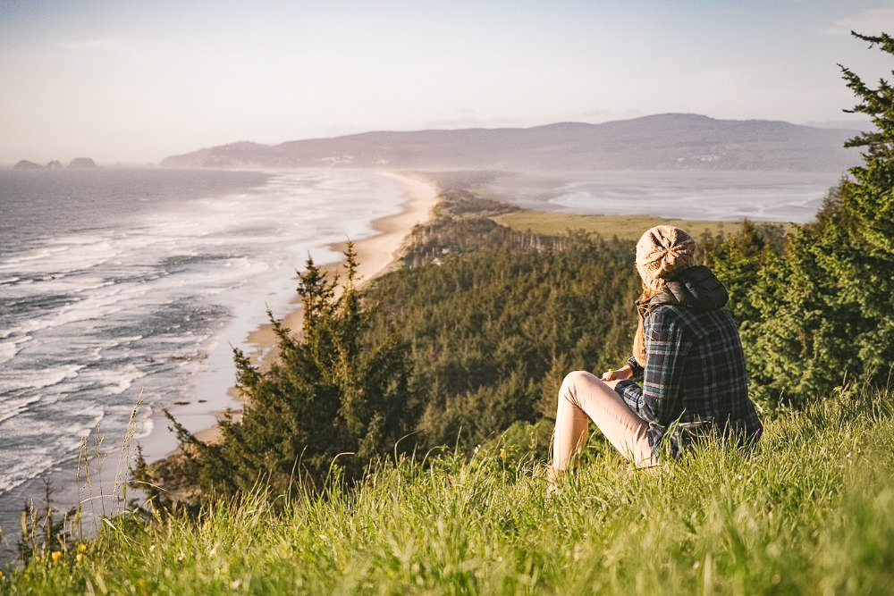 woman sitting on a hill overlooking trees and the ocean.