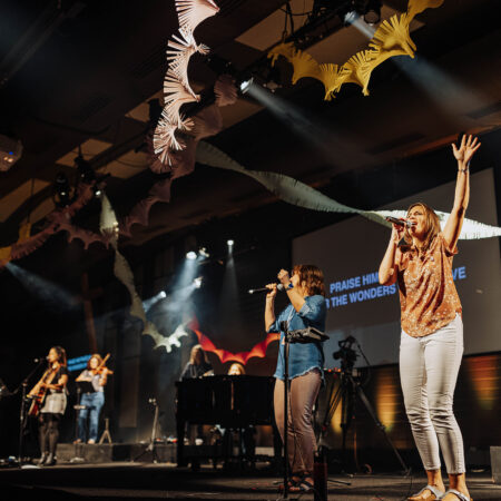 women on stage with band worshiping